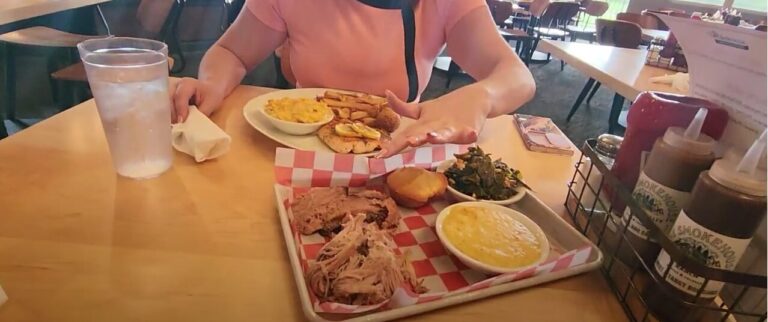 A plate of grilled salmon with lemon, hush puppies, french fries, and creamed corn, alongside a plate of brisket, pulled pork, cheesy grits, collard greens, and cornbread