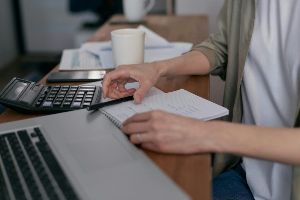 a person sitting next to a table with calculator, notebook and a laptop